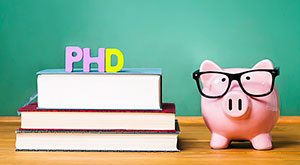 PhD degree theme with textbooks and piggy bank with glasses on green chalkboard background